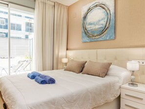 A hotel room with a bed, a nightstand, a lamp, a painting, and a view of the outside. - Ciudad Jardin II by Interhome (Oropesa del Mar)