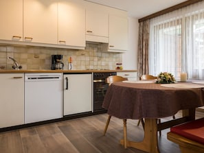 A modern kitchen with white cabinets, a coffee maker, and a dining area with a table and chairs. - Haus Adora Appartement/Fewo 5-Bettwohnung Nr. 5 by Interhome (Saas-Almagell)