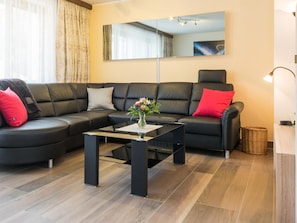 Ein modernes Wohnzimmer mit einem schwarzen Ledersofa, einem Couchtisch und einem Spiegel an der Wand.