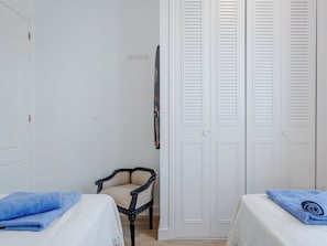 A room with two beds, a chair, and a white door with louvered shutters. - Club Sevilla I by Interhome (Oliva)