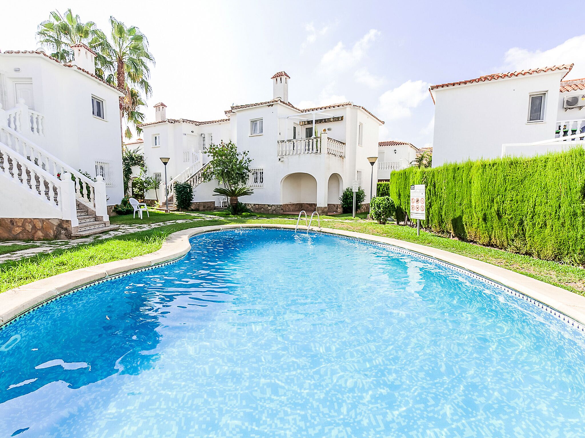 Una piscina de borde curvo, rodeada por edificios blancos con ventanas arqueadas y un balcón.