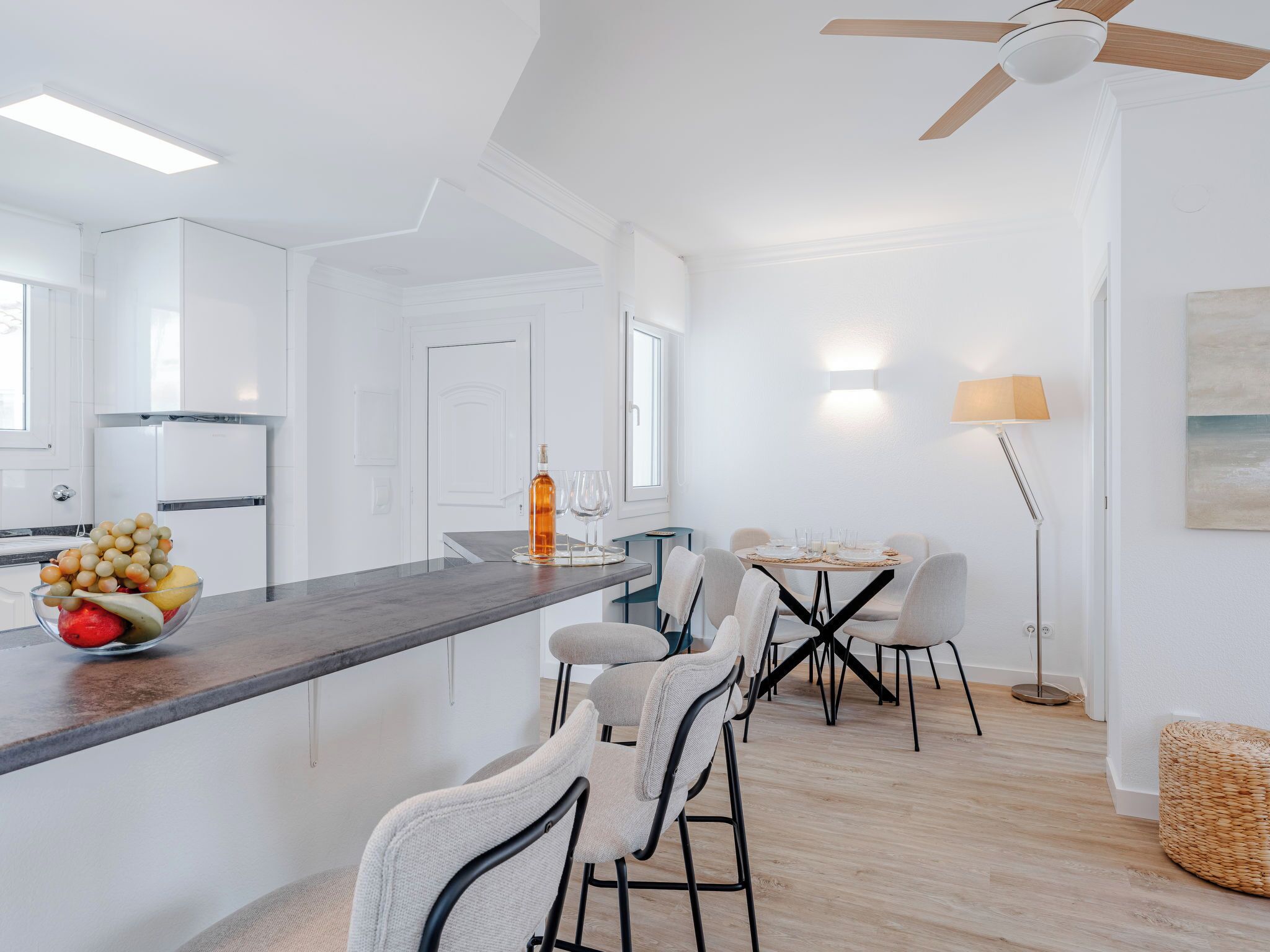 A modern kitchen with white cabinetry, a bar area with stools, a dining table set for four, and a ceiling fan.