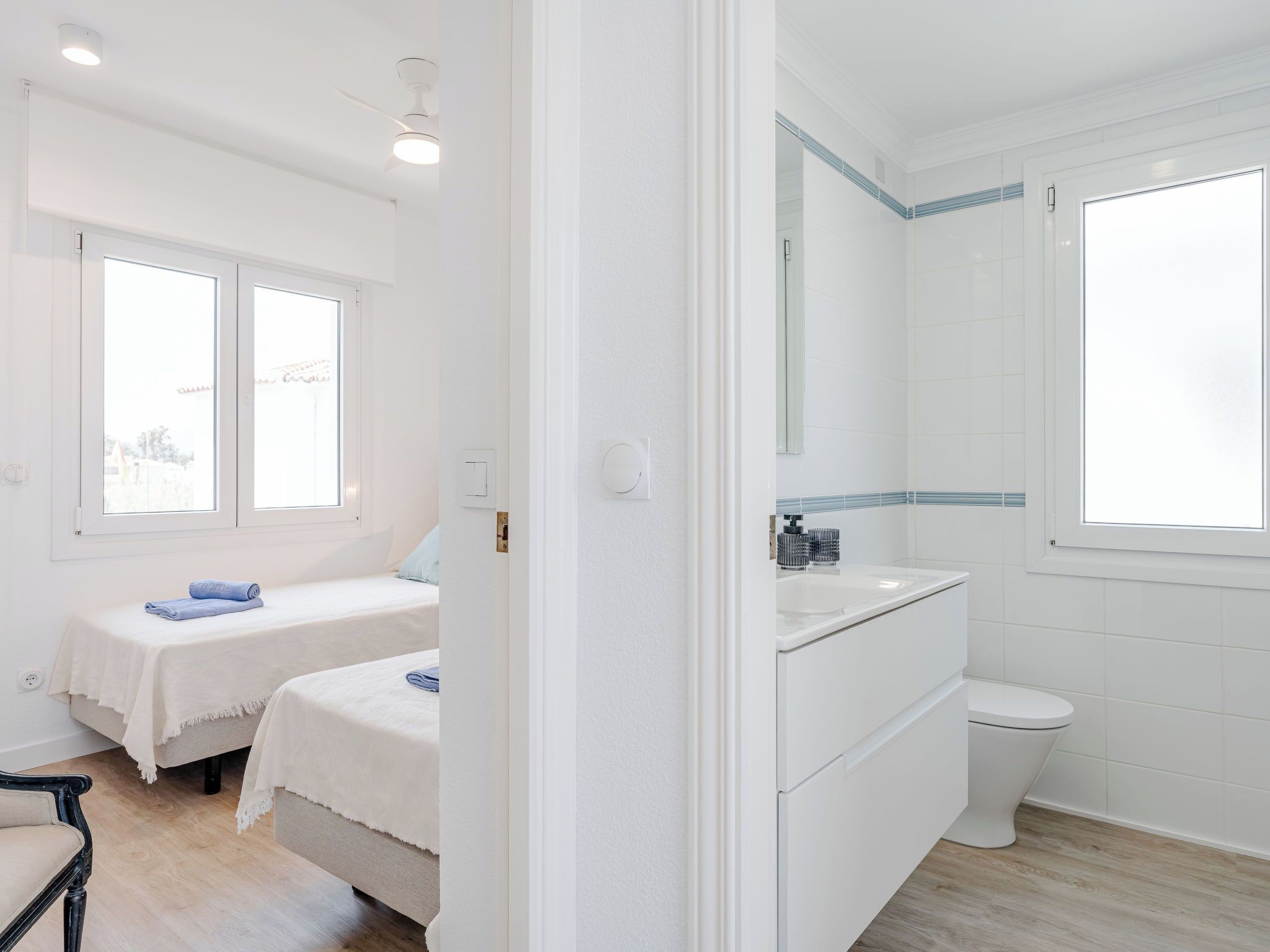 Una habitación con una cama, una silla, una mesita, una ventana y un baño con inodoro y lavamanos.