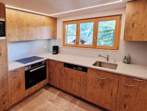 Une cuisine moderne avec des meubles en bois, un lave-vaisselle encastré, une cuisinière et une fenêtre donnant sur les arbres.