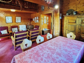 Une pièce chaleureuse avec un décor intérieur en bois, un lit recouvert d’une courtepointe à motifs floraux, deux fauteuils, une petite table et un buffet.