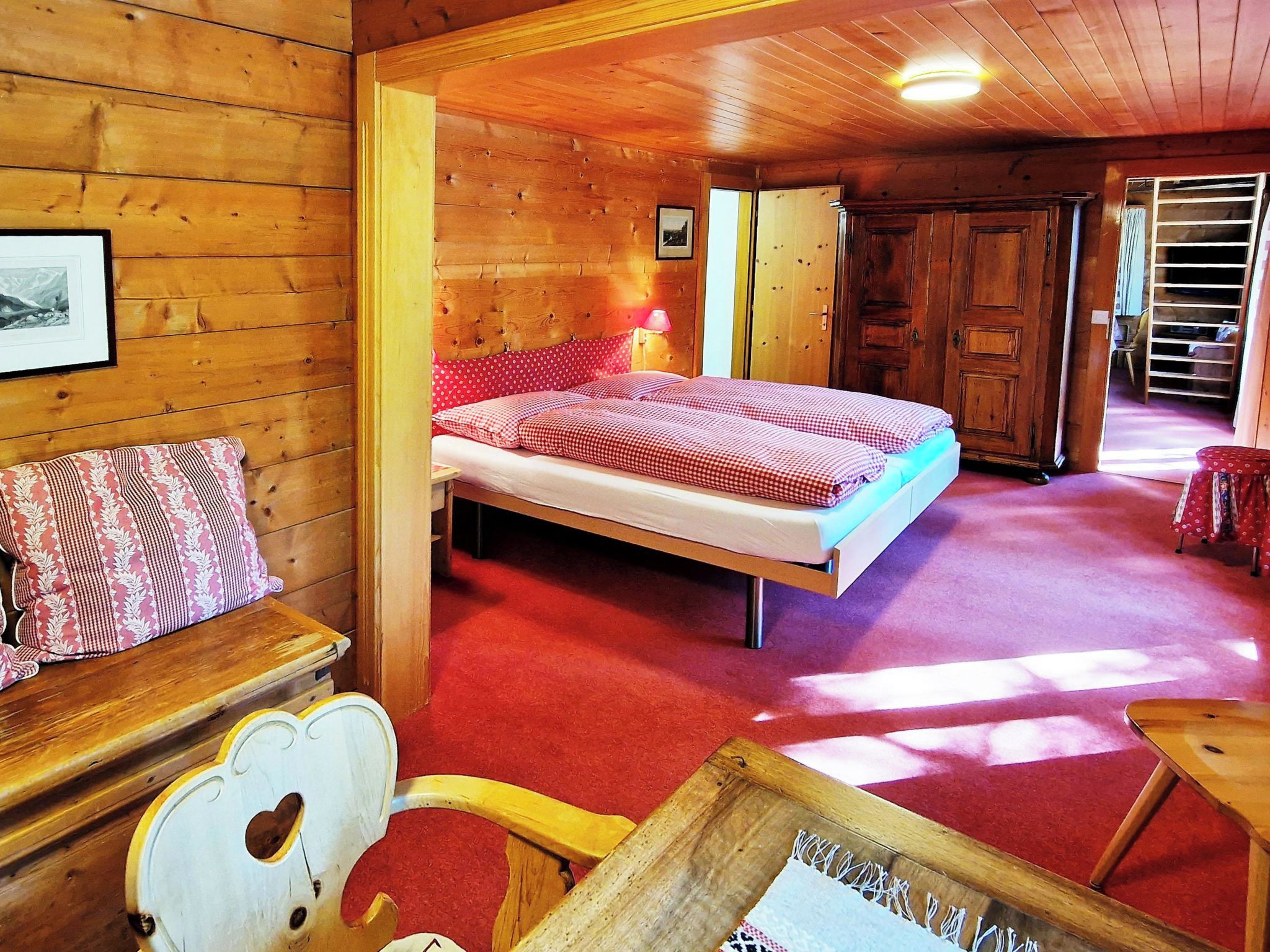 A wooden room with a bed, a wooden chair, and a small table.