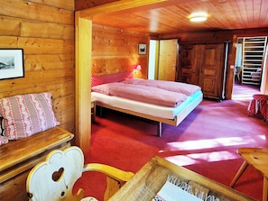 Ein Zimmer mit Holzboden, einem Bett, einem Holzstuhl und einem kleinen Tisch.