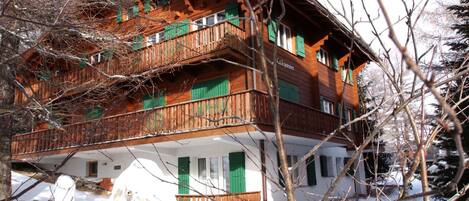 Un immeuble en bois à plusieurs étages, doté de balcons, de volets verts et d’une fondation en pierre.
