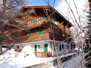 Un immeuble en bois à plusieurs étages, doté de balcons, de volets verts et d’une fondation en pierre.