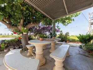 Een terras buiten met een pergola, stenen tafels en banken.