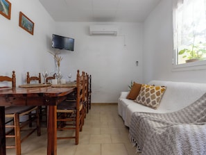 A dining area with a wooden table and chairs, a television mounted on the wall, and a window with a plant. - Vacation home Pepeta by Interhome (Deltebre)