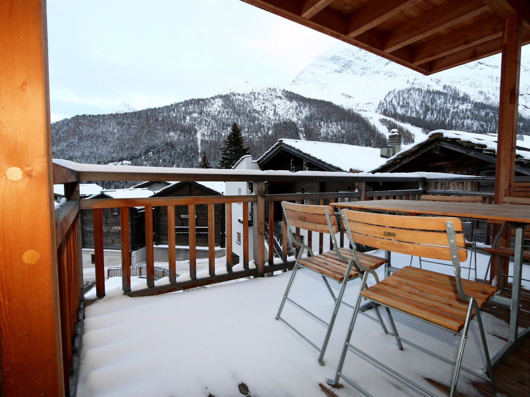 A wooden balcony with metal railings overlooking a snowy mountain landscape.