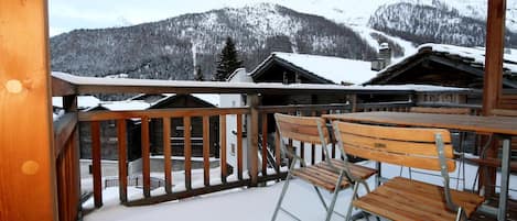 A wooden balcony with metal railings overlooking a snowy mountain landscape.