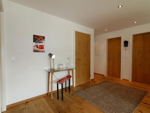 A hallway with wooden flooring, a glass table with a red bench, a wall-mounted lamp, and a door with a clock. - Symbiose Appartement/Fewo, Dusche und Bad, WC, 3 Schlafräume by Interhome (Saas-Fee)
