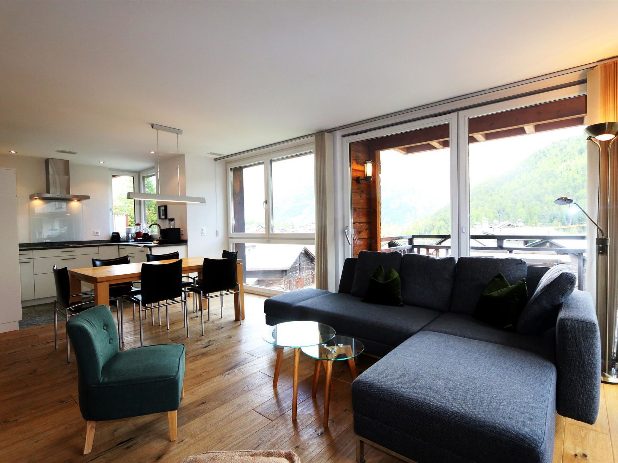A modern interior with a dining area, sofa, and large windows offering a view of the outdoors.
