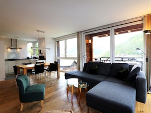 A modern interior with a dining area, sofa, and large windows offering a view of the outdoors. - Symbiose Appartement/Fewo, Dusche und Bad, WC, 3 Schlafräume by Interhome (Saas-Fee)