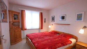 Une chambre à coucher avec un lit en bois, une table de chevet, une commode et une fenêtre avec des rideaux.