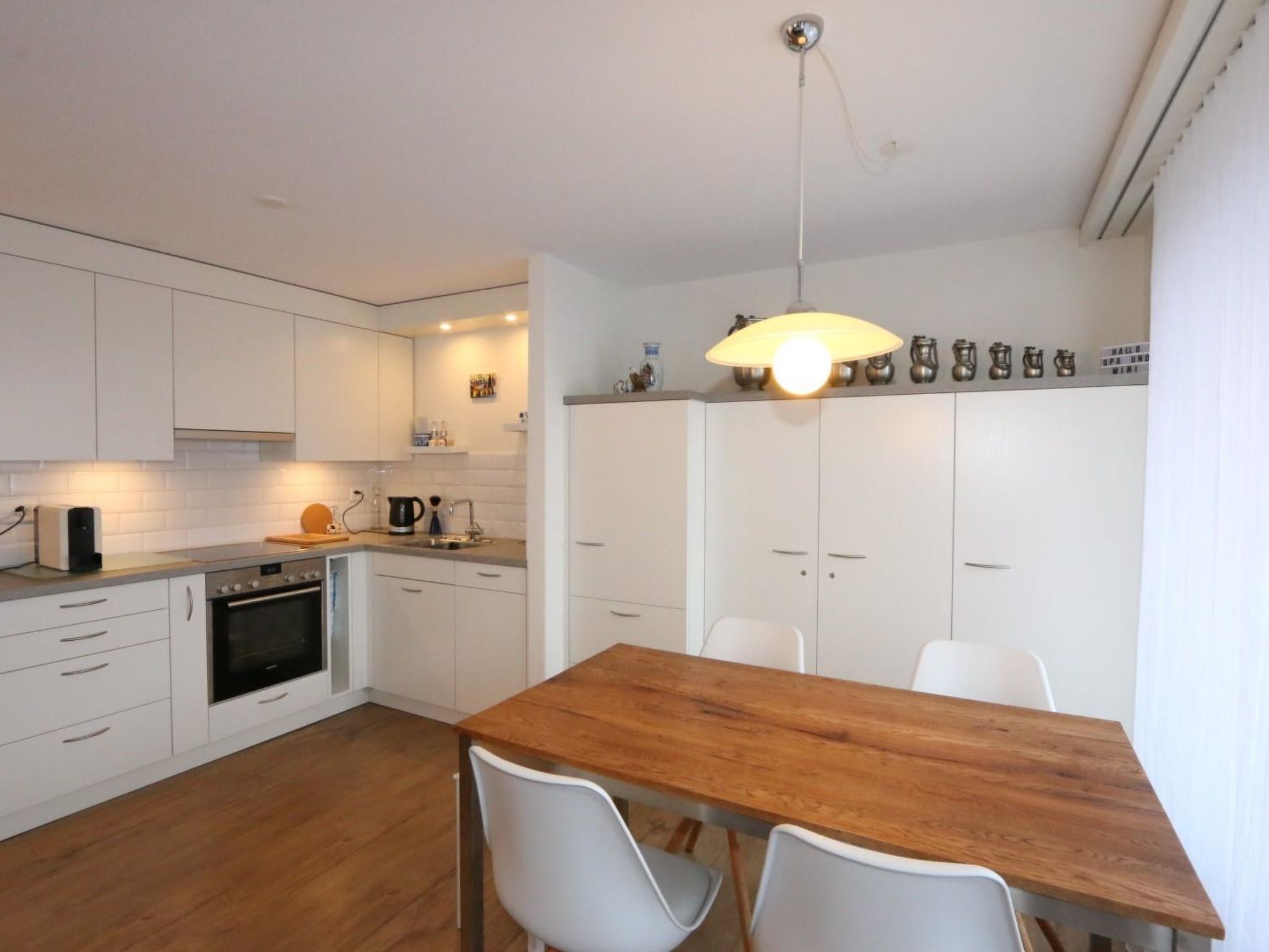 Une cuisine moderne avec des meubles blancs, une table à manger en bois et un luminaire suspendu.