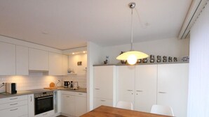 Une cuisine moderne avec des meubles blancs, une table à manger en bois et un luminaire suspendu.