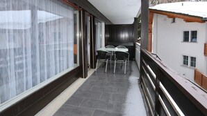 Un balcon avec une table et des chaises, une porte-fenêtre coulissante et une vue sur une montagne enneigée.