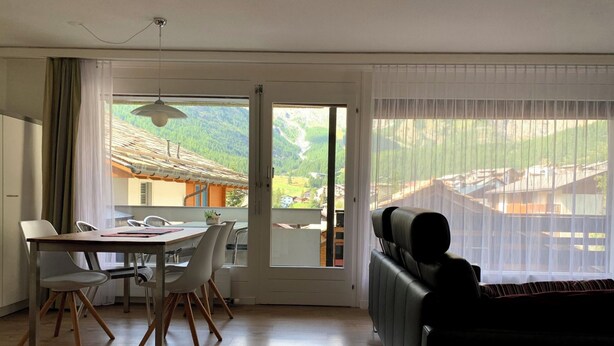 Une pièce comprenant une table à manger, des chaises, un canapé et de grandes fenêtres donnant sur un paysage montagneux.