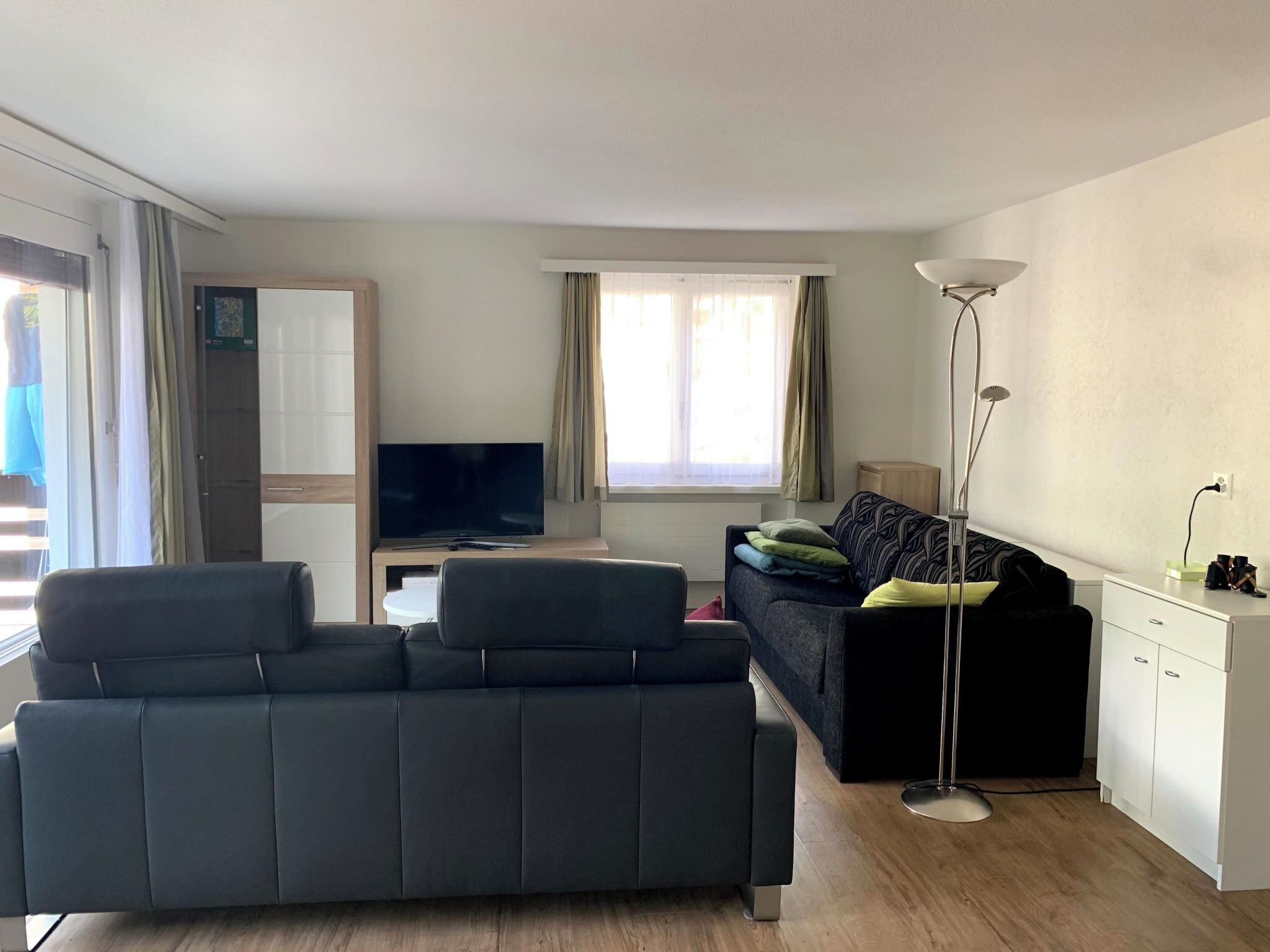 A modern living room with a sofa, a television, a floor lamp, and a window with curtains.