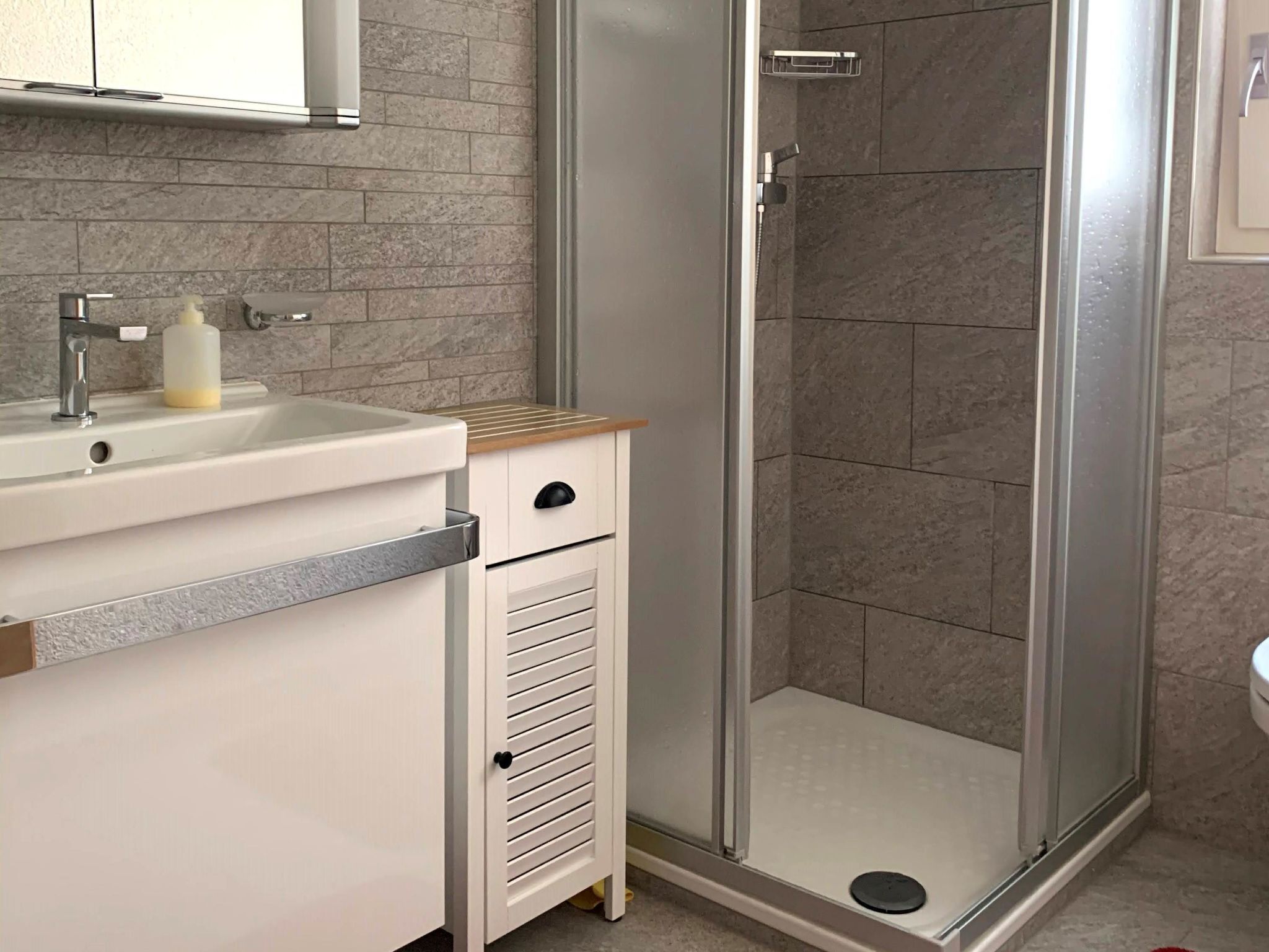 A bathroom with a shower, sink, and storage cabinet.