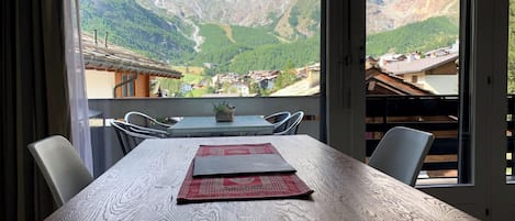 A dining table with chairs, a view of a mountainous landscape, and a wooden deck.