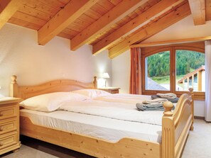 Ein hölzernes Bett in einem Zimmer mit Blick auf eine Berglandschaft durch ein großes Fenster.