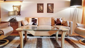 Ein Wohnzimmer mit einem Glastisch, einer Couch mit Kuhlederkissen, Holzboden und zwei gerahmten Bildern an der Wand.