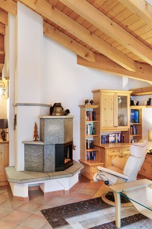 Ein gemütliches Wohnzimmer mit Kamin aus Stein, Holzregalen, einem weißen Sessel und einem Glastisch.