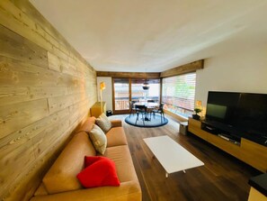 A modern living room with a wooden wall, a sofa with cushions, a dining area with a table and chairs, and a TV on a stand. - Waldrain 5 Appartement/Fewo Appartement/Fewo by Interhome (Saas-Fee)