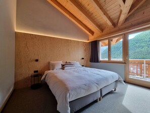 Et soveværelse med en stor seng, trævægge, et vindue med udsigt til en skov og en balkon.