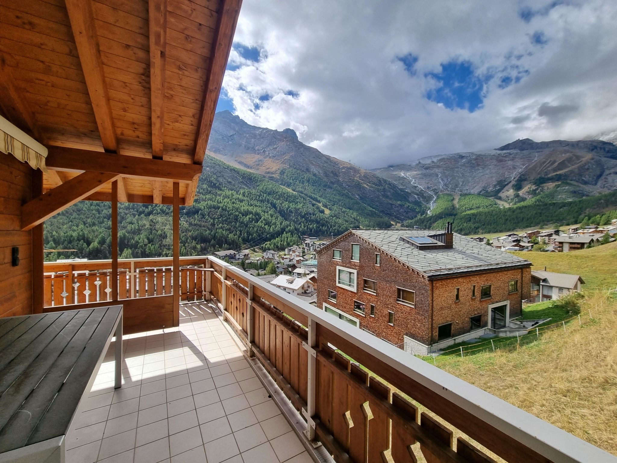 Un balcón de madera con suelo de baldosas, con vistas a un pueblo y montañas.