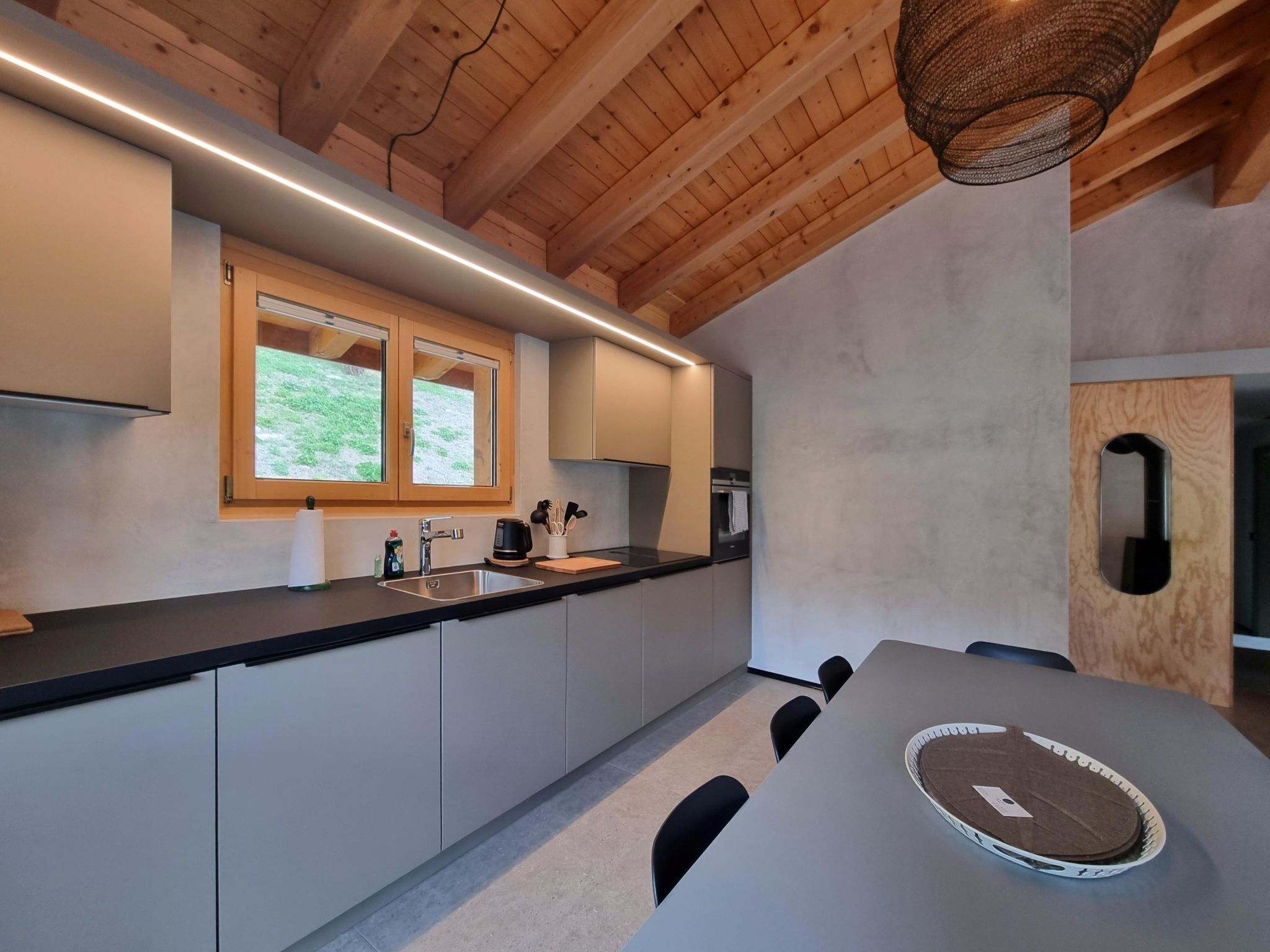A modern kitchen with wooden beams, a window, a sink, and a table with a placemat.
