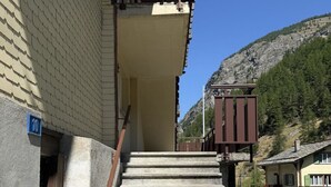 A set of concrete steps leading to a building with a metal railing and a blue sign indicating the number 10. - Bergtreu Appartement/Fewo 4-Bettwohnung by Interhome (Saas-Balen)