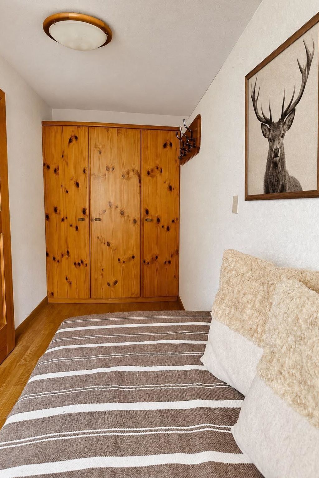 Um quarto com tapete listrado, guarda-roupa de madeira e um quadro de um veado na parede.