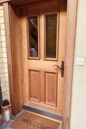 Puerta de madera con panel de vidrio, felpudo y farol.