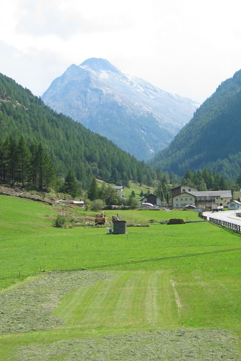 Ländliche Landschaft mit einem Berg im Hintergrund, einem grünen Feld und einigen Gebäuden.
