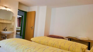 Hotellihuone, jossa on sänky, yöpöytä lampun kanssa, kylpyhuone, jossa on pesuallas ja peili, sekä ovi, joka johtaa toiseen huoneeseen.