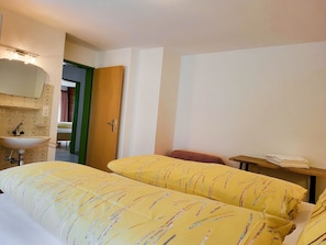 A hotel room with a bed, a bedside table with a lamp, a bathroom with a sink and mirror, and a door leading to another room. - Apartments Atlas Appartement/Fewo Atlas 3 by Interhome (Saas-Grund)