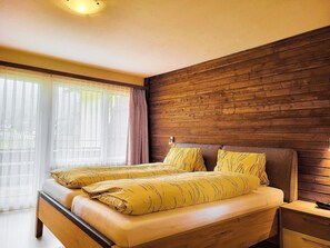 A double bed with a wooden headboard in a room with a large window and a wooden wall. - Apartments Atlas Appartement/Fewo Atlas 3 by Interhome (Saas-Grund)