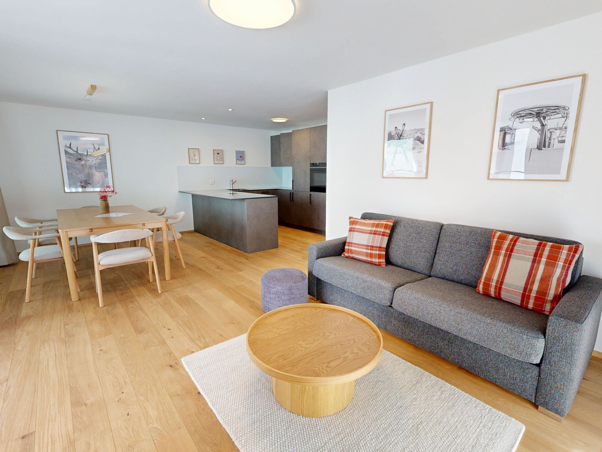 Una sala de estar moderna con un sofá gris, una mesa de comedor de madera y una cocina al fondo.