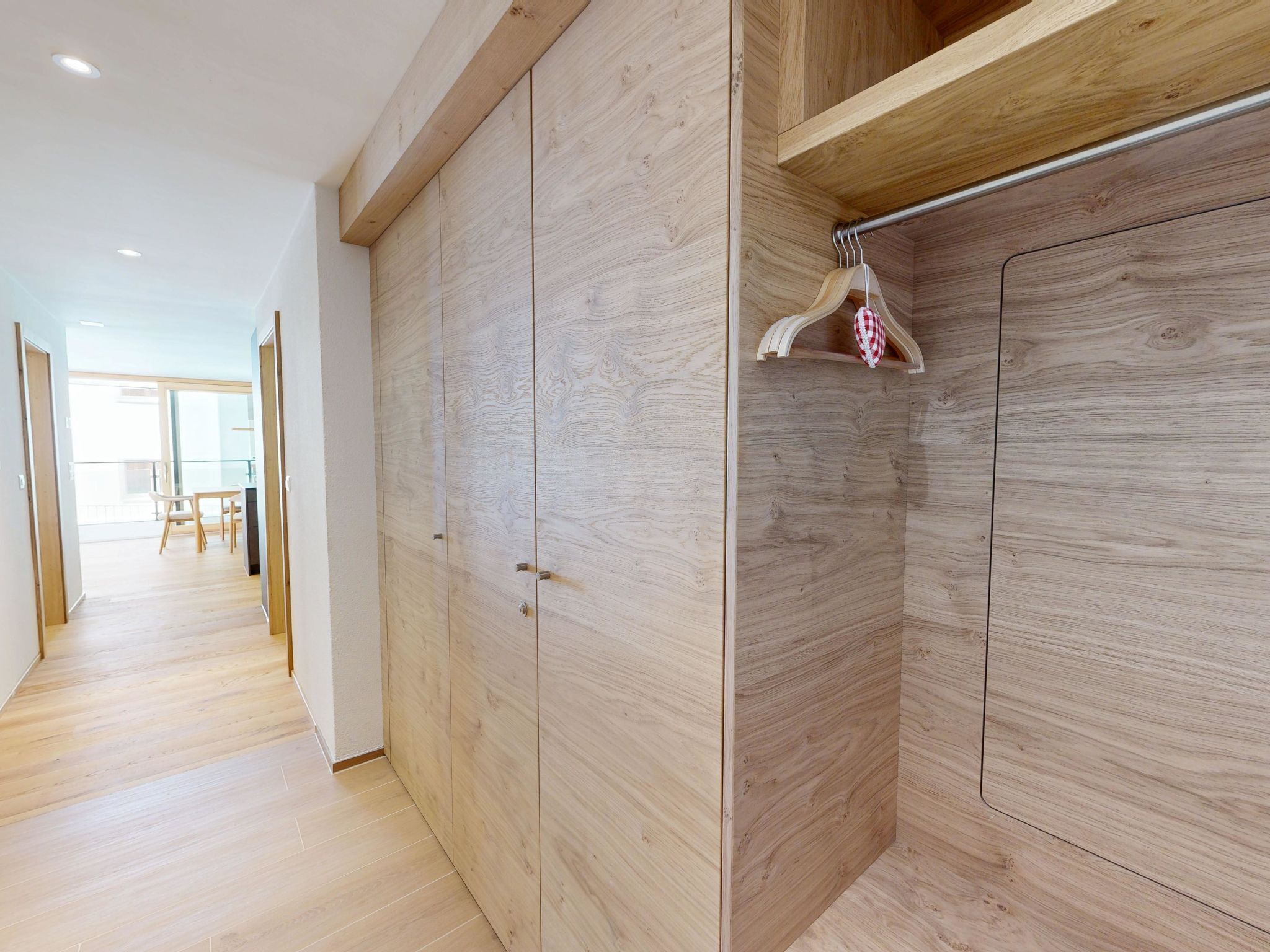 Un intérieur moderne avec un plancher en bois, un couloir menant à une pièce dotée d’une grande armoire et d’un portant à vêtements.