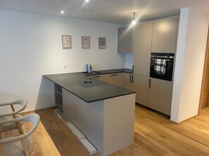 A modern kitchen with a central island, a built-in oven, and a sink. There are three framed pictures on the wall. - Alphubel Peak & Unlimited Appartement/Fewo Peak 03 by Interhome (Saas-Fee)