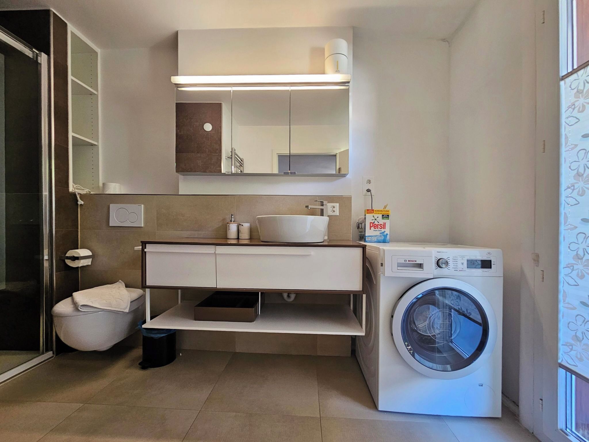 Un baño pequeño con lavadora, lavamanos y espejo sobre el mueble.