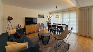Ein modernes Wohnzimmer mit einer Couch, einem Fernseher, einem Esstisch, Stühlen und einer Stehlampe.