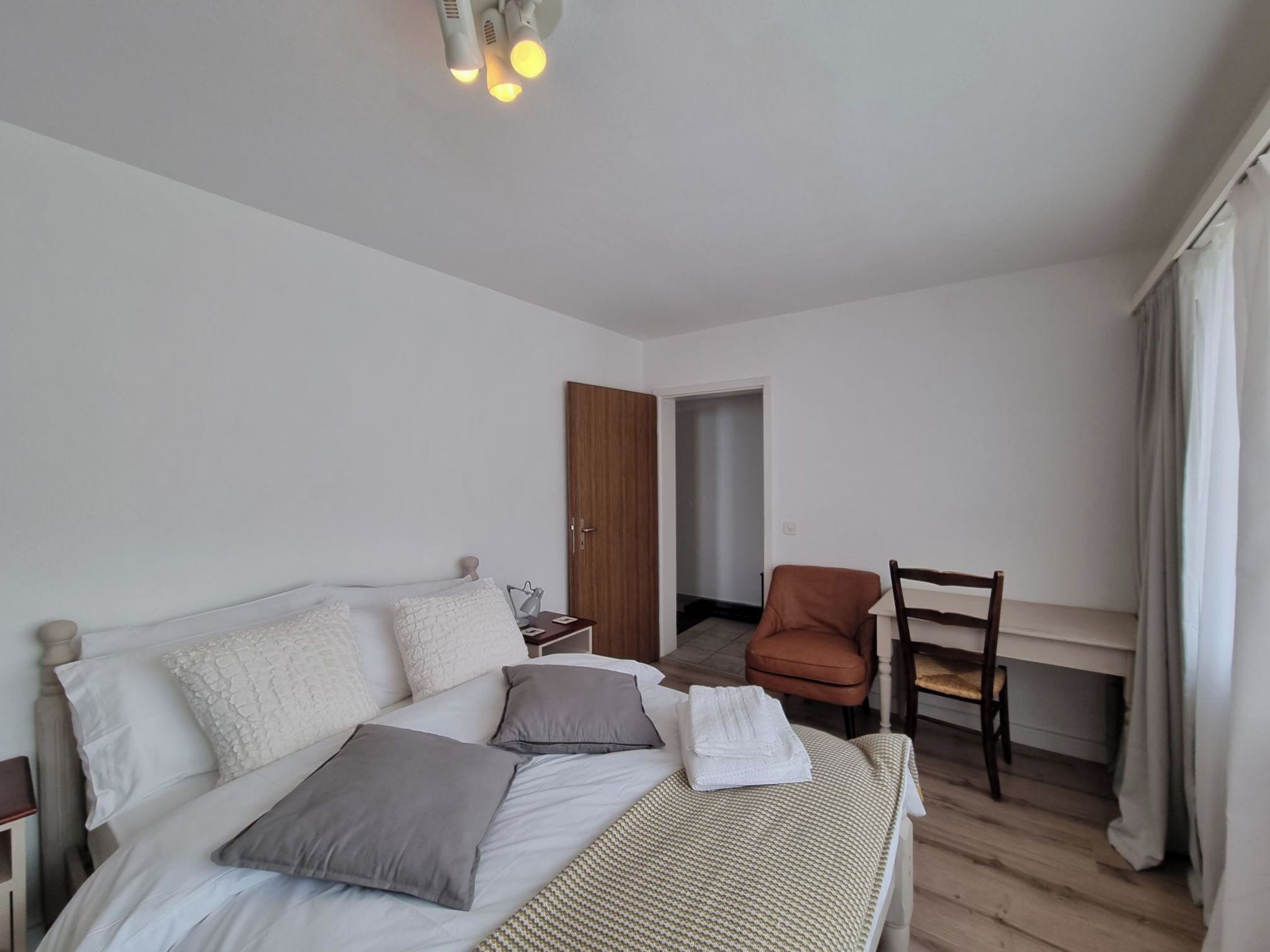 Une chambre à coucher comprenant un lit, un bureau, une chaise et une porte donnant sur une autre pièce.