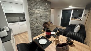Une cuisine moderne avec des meubles blancs, un mur en pierre et un coin repas comprenant une table en bois, des sièges en cuir noir et une cheminée.