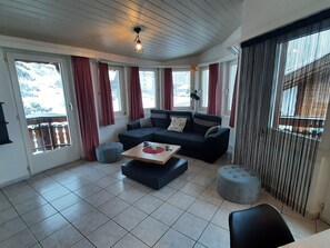 Ein Wohnzimmer mit einem Ecksofa, Poufs, einem Couchtisch und einer Deckenleuchte.